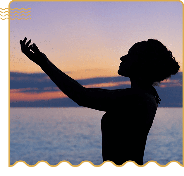 A woman standing in front of the ocean at sunset.