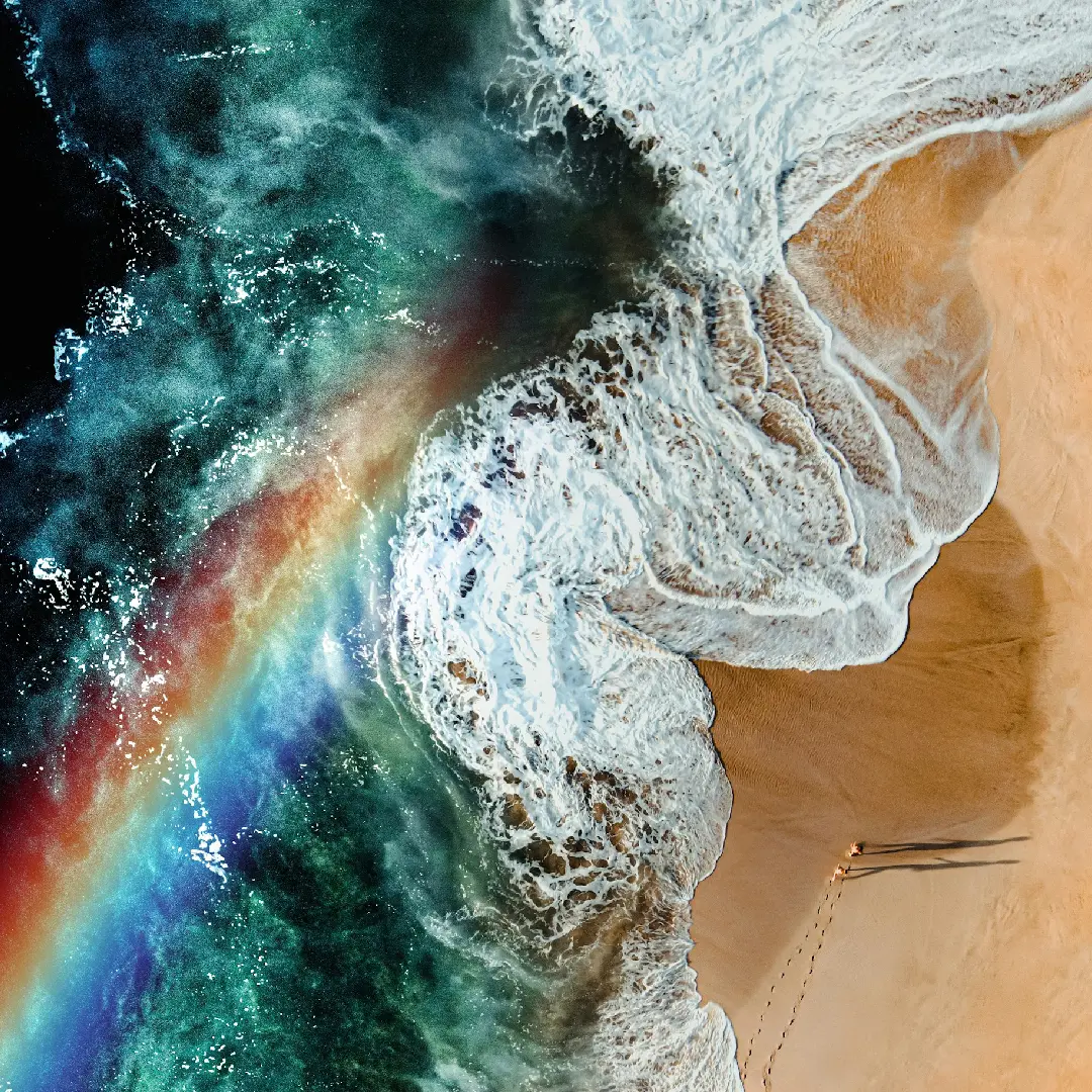 A rainbow is seen in the water near the beach.